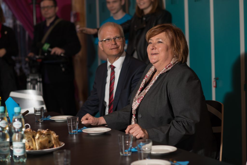 Anna Komorowska i Piotr Litwa podczas rozmowy przy stole w Centrum Zimbardo w Nikiszowcu. W tle reporterzy.