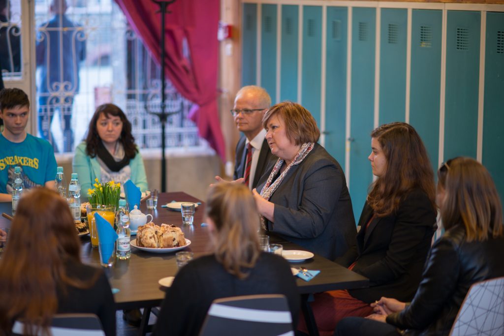 Grupa os&oacute;b siedzi przy stole, gł&oacute;wna postać Anna Komorowska.