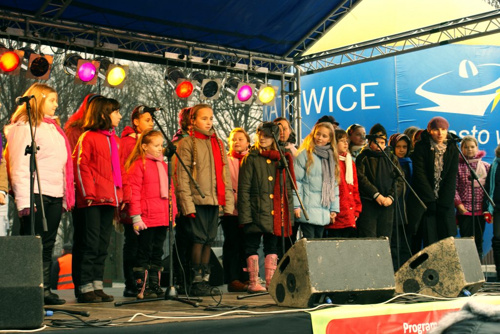 Grupa dzieci z nauczycielką w trakcie występu na scenie.