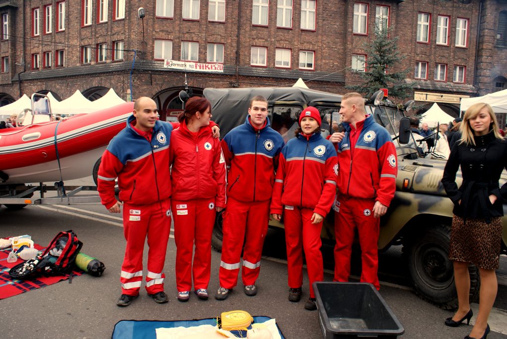 Grupa ratownik&oacute;w medycznych w czerwono-niebieskich strojach, przed nimi leży fantom.