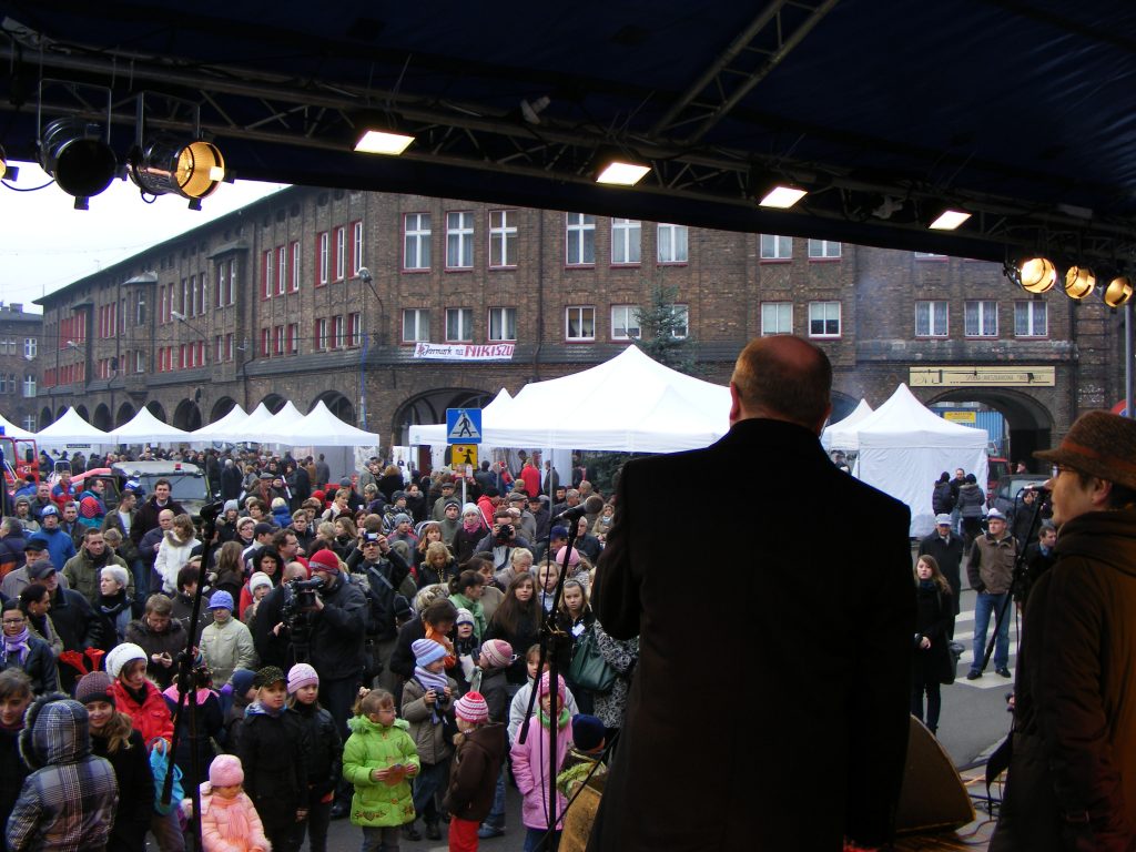 Widok ze sceny na tłum ludzi zgromadzonych na placu Nikoszowca. Na pierwszym planie stoi mężczyzna, kt&oacute;ry przemawia.