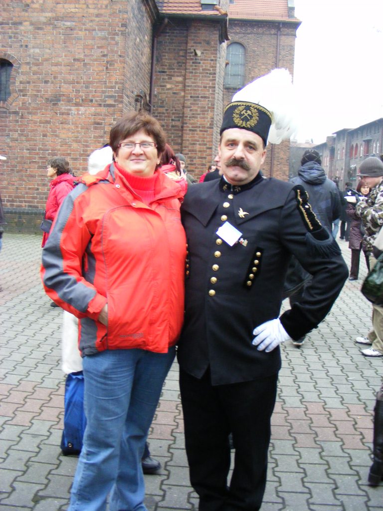 Mężczyzna w galowym stroju g&oacute;rnika pozuje do zdjęcia z kobietą. W tle inne osoby.