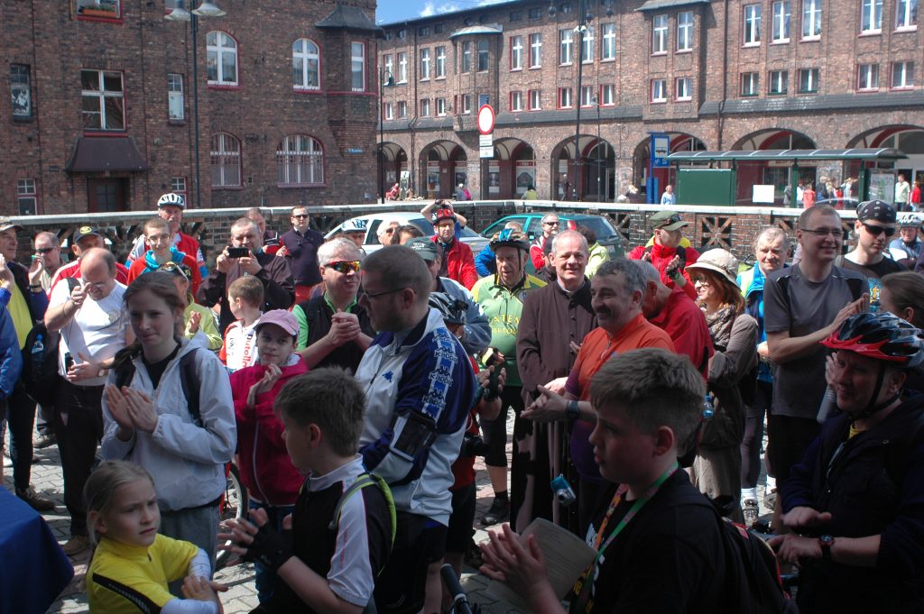 Tłum ludzi zgromadzony prawdopodobnie przed makietą osiedla Nikiszowiec. W tle ceglane budynki.