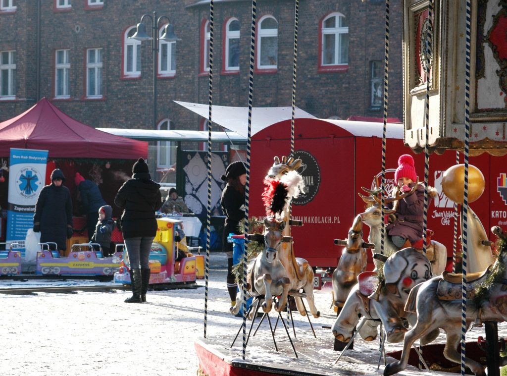 Dziecko siedzi na reniferze zabytkowej karuzeli. W tle inne dziecko przy kolorowej kolejce.