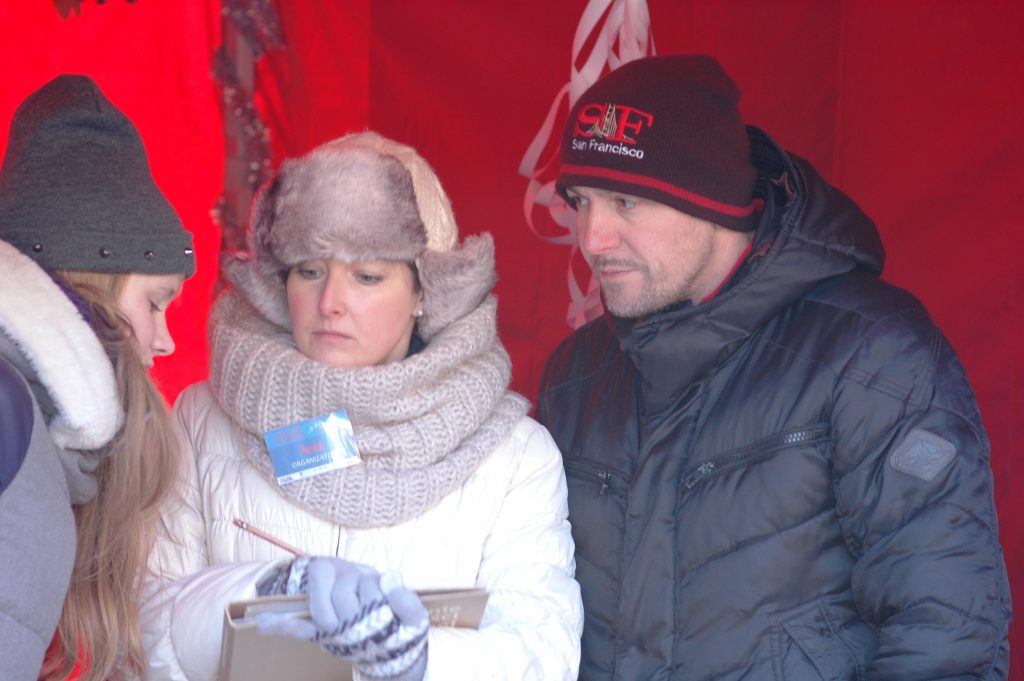 Trzy osoby rozmawiają, jedna z nich ma plakietkę organizatora, stoją w czerwonym namiocie.