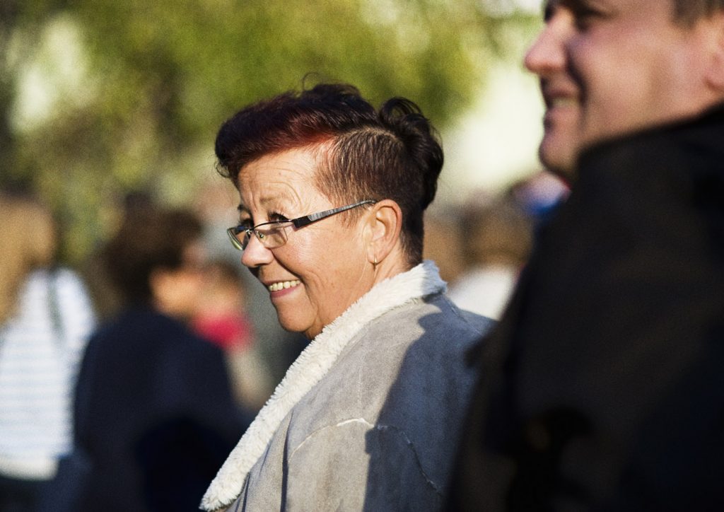 Uśmiechnięta kobieta w okularach ogląda się przez ramię. Przed nią nieostra postać mężczyzny.