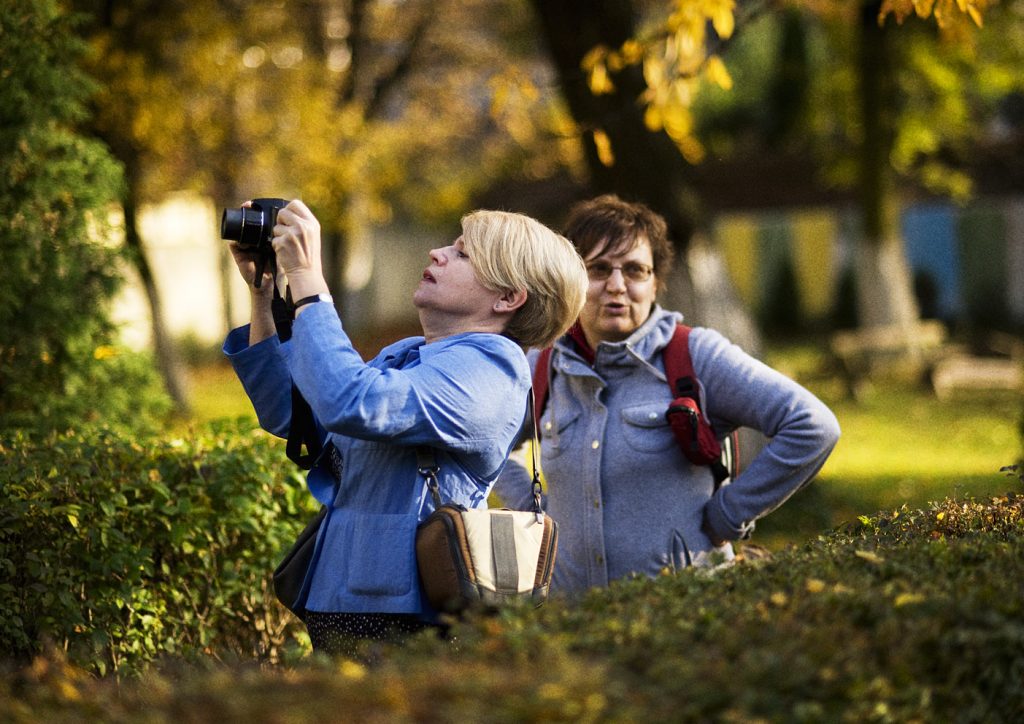Dwie kobiety w jesiennym parku. Jedna z nich robi zdjęcie aparatem.