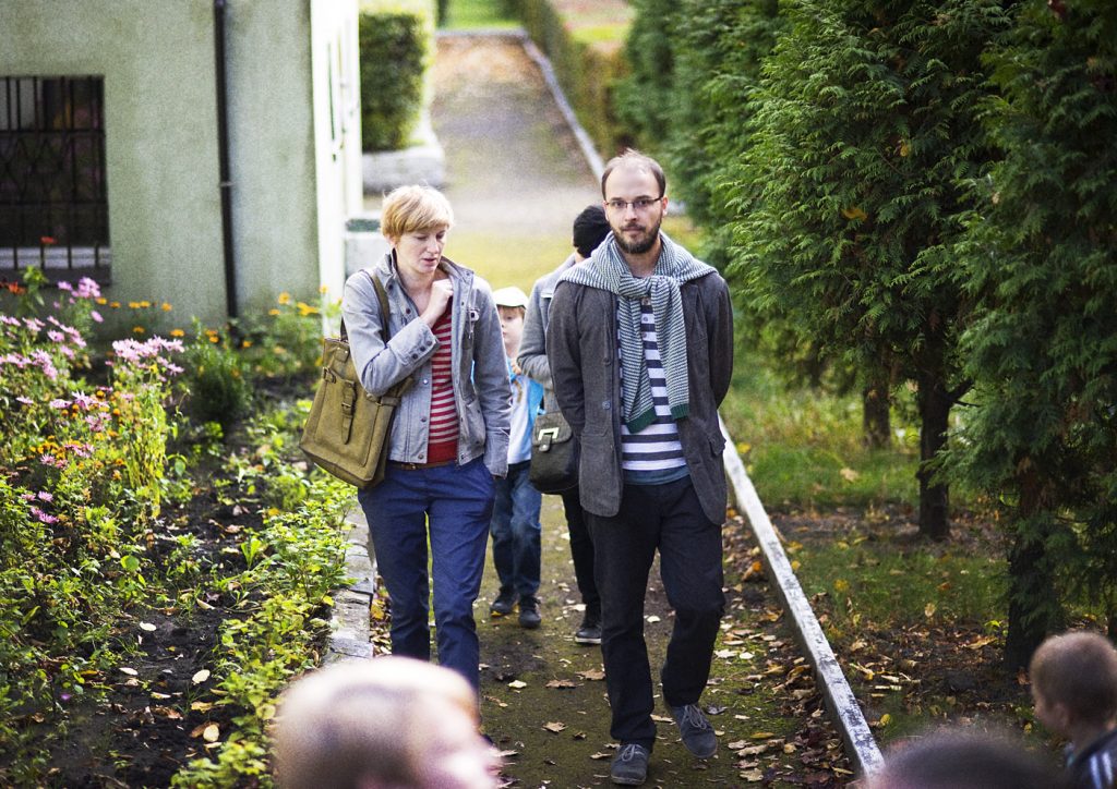 Kobieta i mężczyzna spacerują parkową alejką.. W tle widać małego chłopca.
