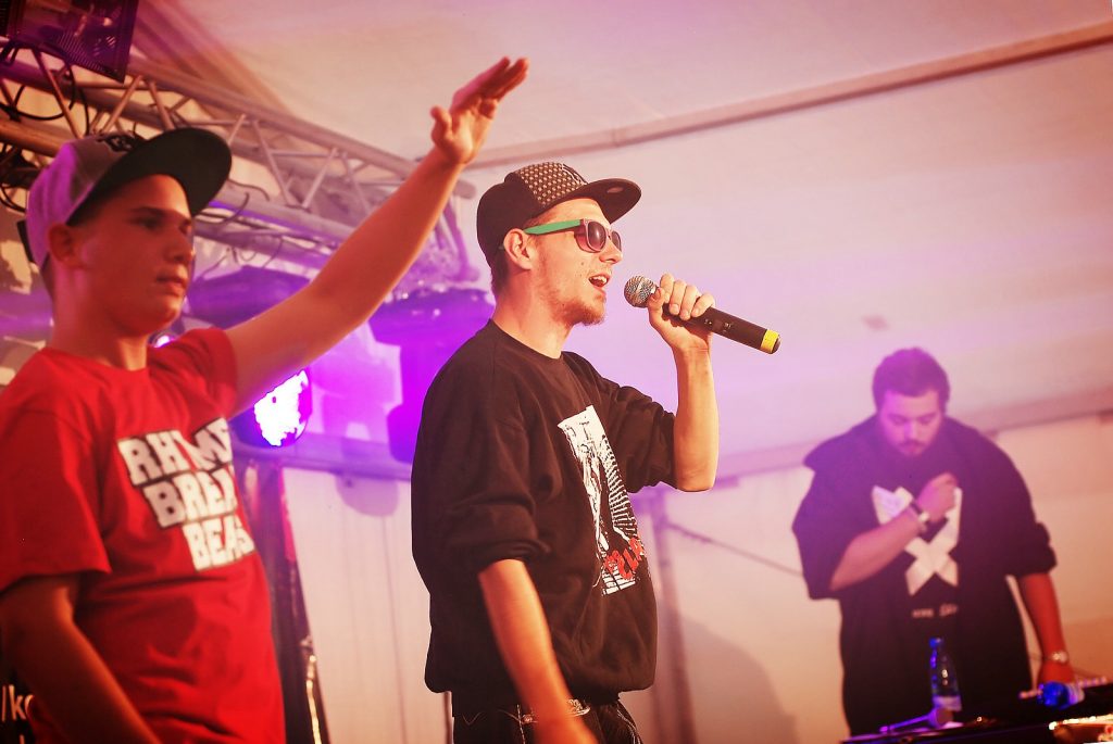 Trzech mężczyzn na scenie, jeden z nich śpiewa do mikrofonu.