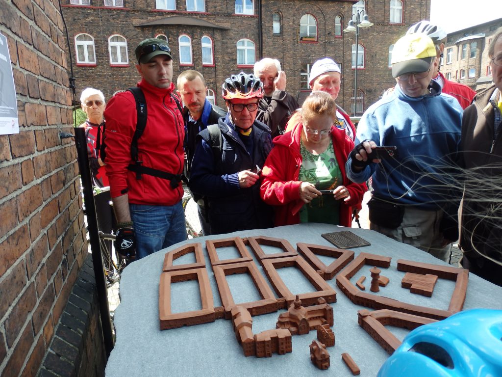 Grupa rowerzyst&oacute;w fotografuje makietę osiedla Nikiszowiec.