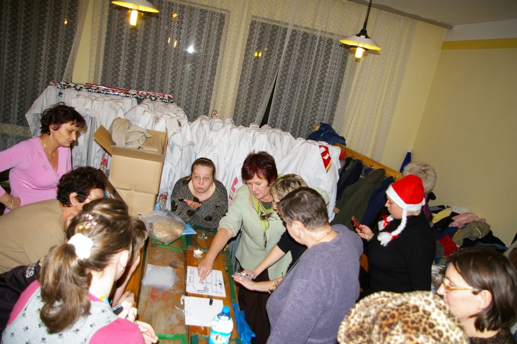 Grupa kobiet dyskutuje nad rozkładem stoisk na jarmarku, w tle złożone białe namioty wystawowe.